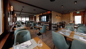 A restaurant with wooden tables, green upholstered chairs, and a bar area with wine bottles. - BERG&BERG APARTMENTS-Spiez Self Check-In (Spiez)