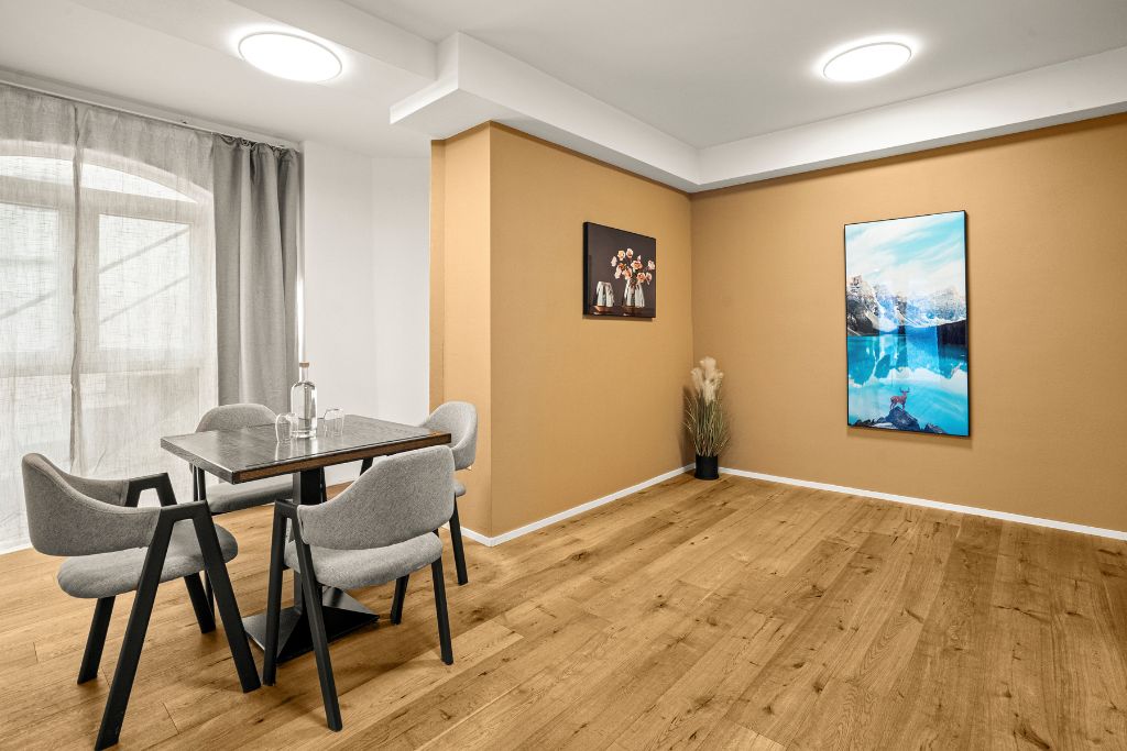 Un salón de conferencias con piso de madera, una mesa con sillas y dos obras de arte enmarcadas en la pared.