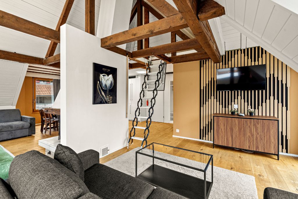 A modern living room with a loft-style ceiling, a dining area, and a kitchen with a TV.