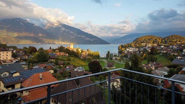 A scenic view of a lakeside town with a prominent church, mountains in the background, and residential buildings. - BERG&BERG APARTMENTS-Spiez Self Check-In (Spiez)