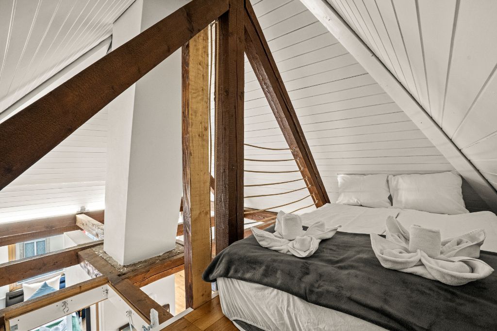 Een slaapkamer met een schuine kap, een bed met een donkere deken en uitzicht op het exterieur.