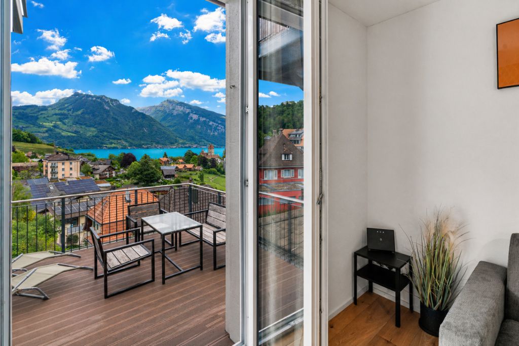 Un balcon avec vue sur un lac et des montagnes, un canapé, une petite table et une plante en pot.
