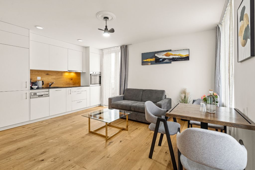 A modern kitchen with white cabinets, a wooden countertop, and a dining area with a glass table and grey chairs.