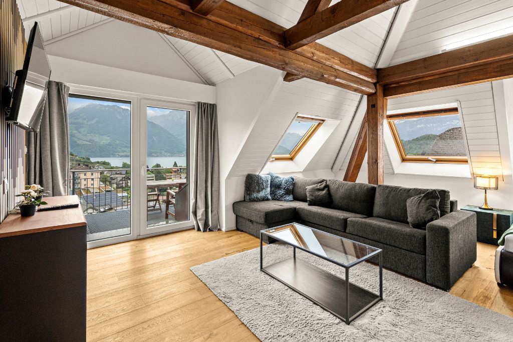 A modern living room with a sofa, a coffee table, and a view of a lake and mountains through large windows.
