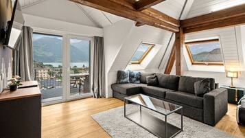 A modern living room with a sofa, a coffee table, and a view of a lake and mountains through large windows.