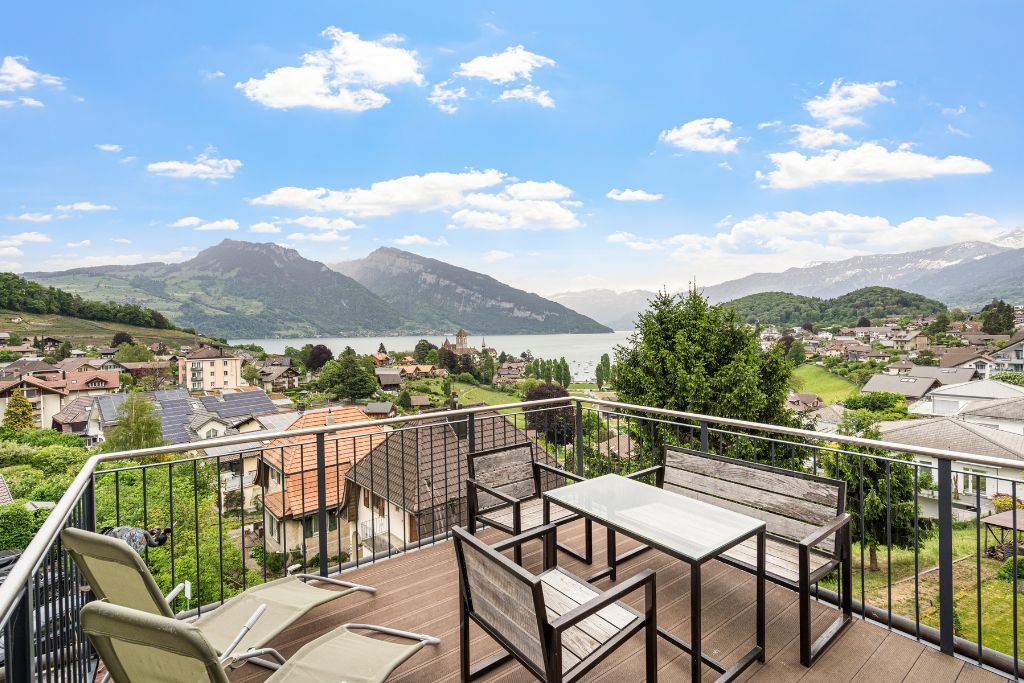 A balcony with a table and chairs overlooking a lake and mountains.