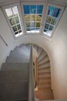 Una escalera de caracol con cerramiento de vidrio en la parte superior, que conduce a una plataforma con vistas a la vegetación exterior.