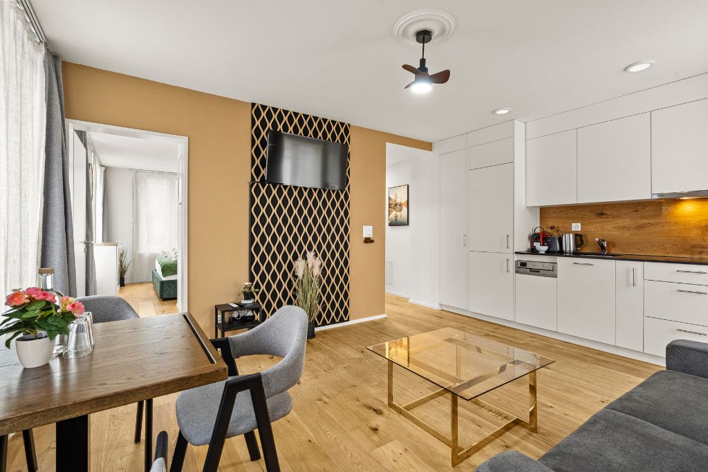 Una sala de estar moderna con comedor, cocina y televisor montado en la pared.