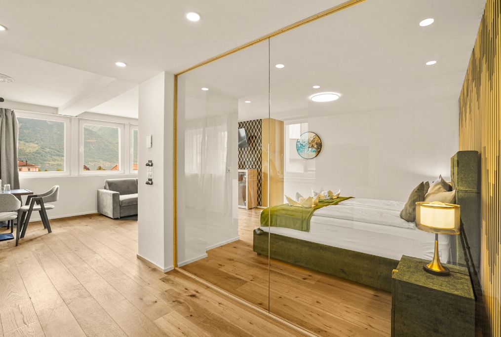 A modern bedroom with a bed, bedside table, and a view of the outdoors through a window.
