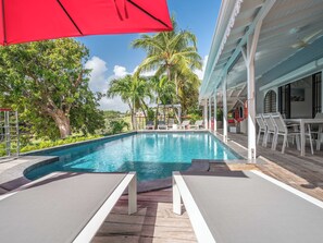A pool area with lounge chairs and umbrellas, surrounded by palm trees and a covered seating area.