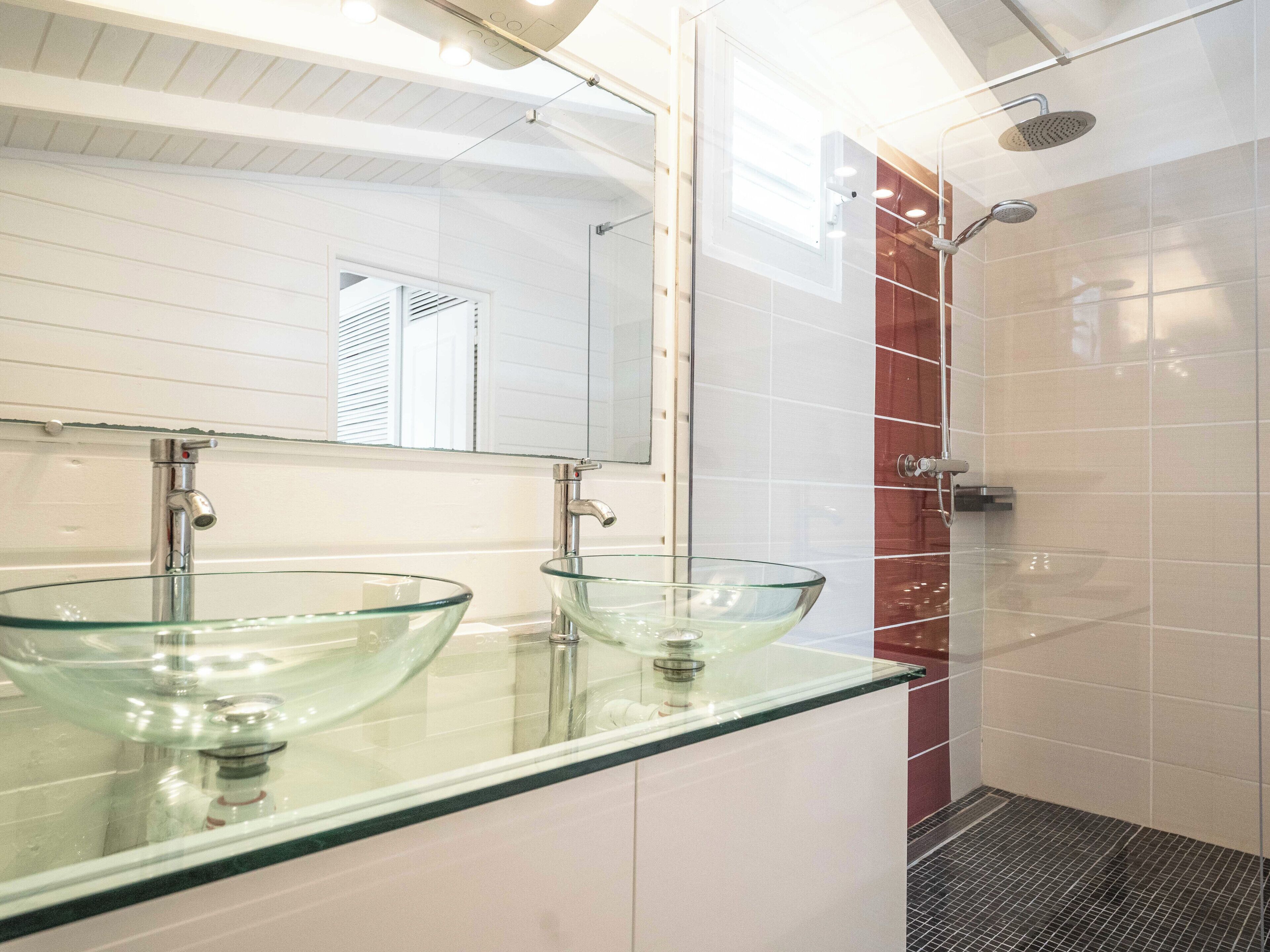 A modern bathroom with two glass sinks, a large mirror, and a shower area.