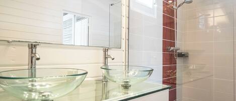 A modern bathroom with two glass sinks, a large mirror, and a shower area.