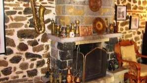 A cozy room with a stone wall, a fireplace, and a variety of decorative items including a saxophone, pottery, and framed pictures. - Guesthouse Bujtina Leon  (Korçë)