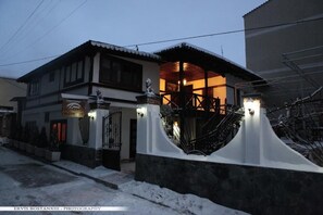A two-story building with a covered entrance and a stone wall. - Guesthouse Bujtina Leon  (Korçë)