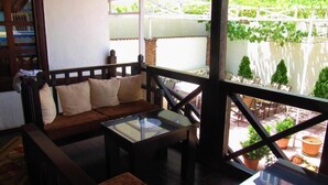 A cozy living area with a sofa, coffee table, and a view of a garden through a balcony. - Guesthouse Bujtina Leon  (Korçë)