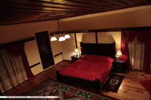 A bedroom with a large bed, two bedside tables with lamps, a patterned rug, and wooden beams on the ceiling. - Guesthouse Bujtina Leon (Korçë)