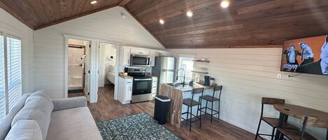 A compact living space with a kitchenette, a sofa, a dining area, and a TV mounted on the wall.