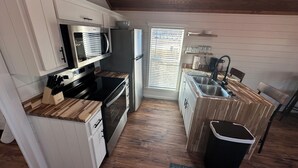 A compact kitchen with white cabinets, a microwave, a refrigerator, a sink, and a trash bin. - Cozy 101 Cabin 1 bdrm on Smith Lake Located beside Smith Lake Park Boat Ramp (Cullman)