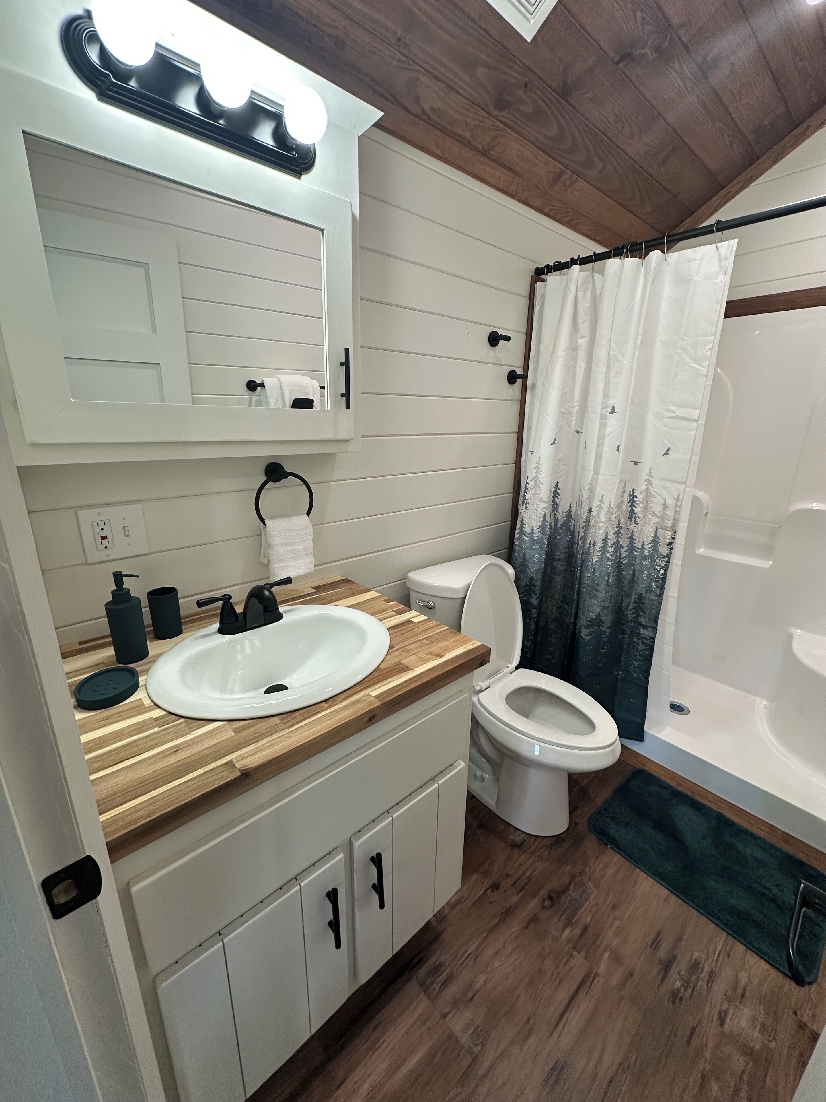 A bathroom with a wooden vanity, white sink, toilet, and a shower with a curtain.