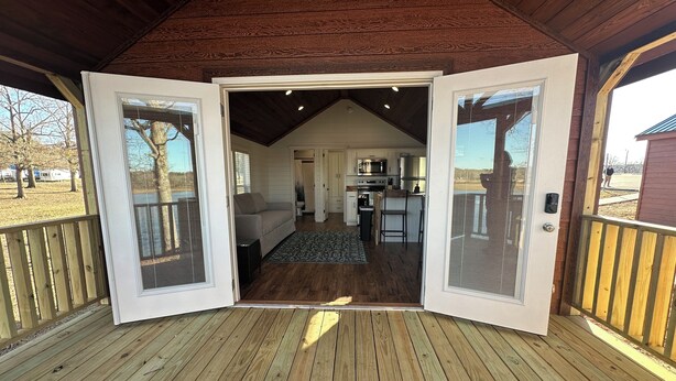 An open wooden deck leading to a living area with a sofa, a kitchen, and a view of the outdoors. - Cozy 101 Cabin 1 bdrm on Smith Lake Located beside Smith Lake Park Boat Ramp (Cullman)