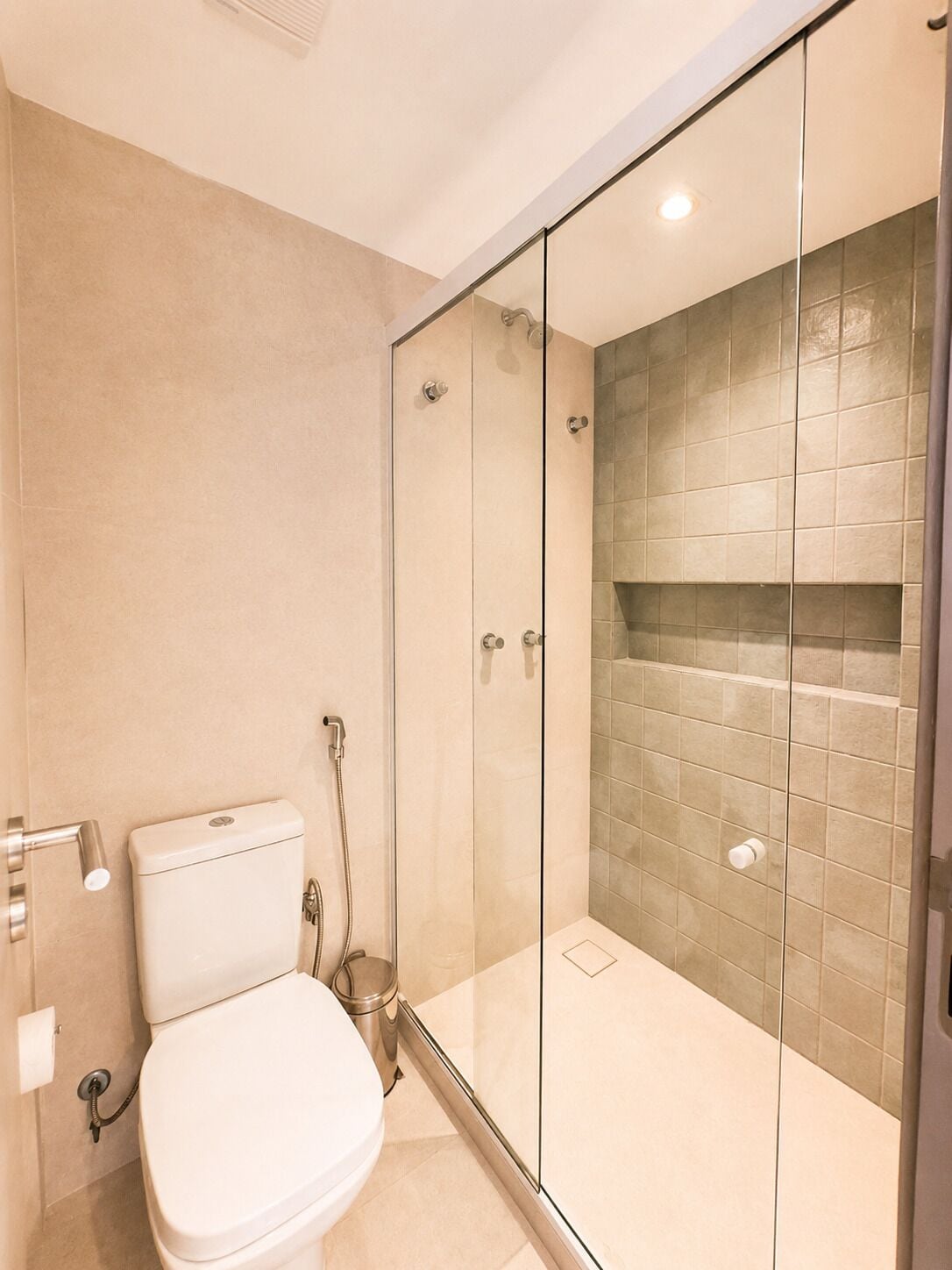 A modern bathroom with a glass-enclosed shower, a toilet, and beige tiled walls.