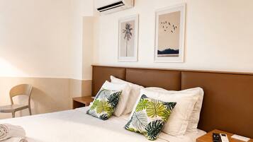 A hotel room with a bed, two pillows with a leaf pattern, a nightstand with a phone, and framed pictures on the wall.