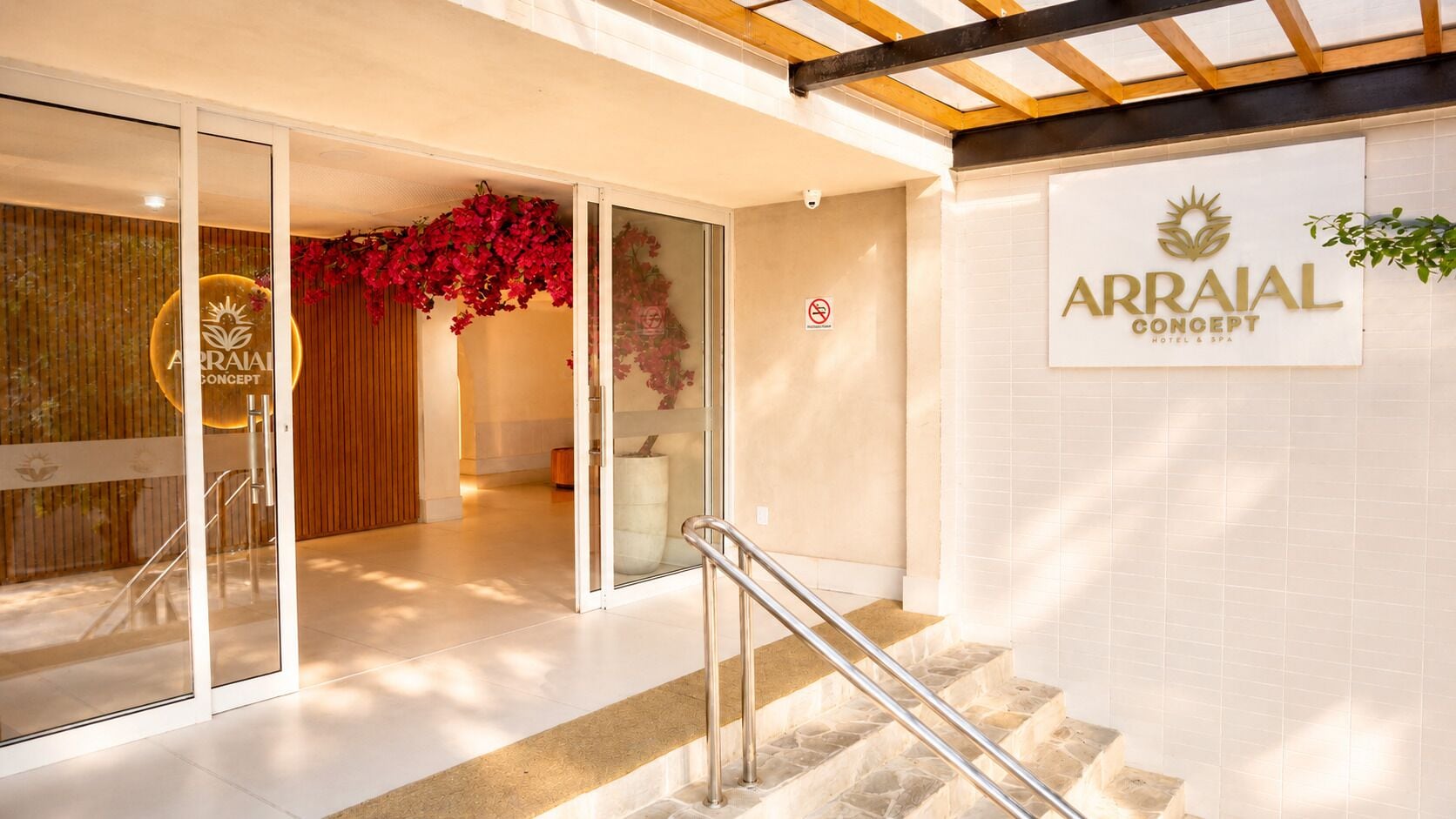 A hotel entrance with a staircase, glass doors, a no-smoking sign, and a sign for Arraial Concept Hotel & Spa.