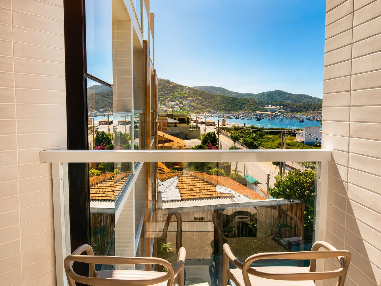 A balcony with a view of a coastal town, a tiled wall, and two chairs.