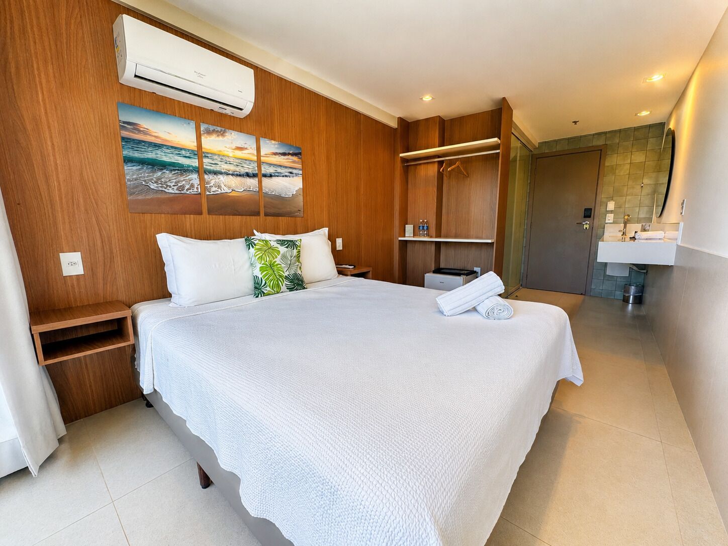 A hotel room with a bed, a wardrobe, a bathroom, and a wall-mounted air conditioner.
