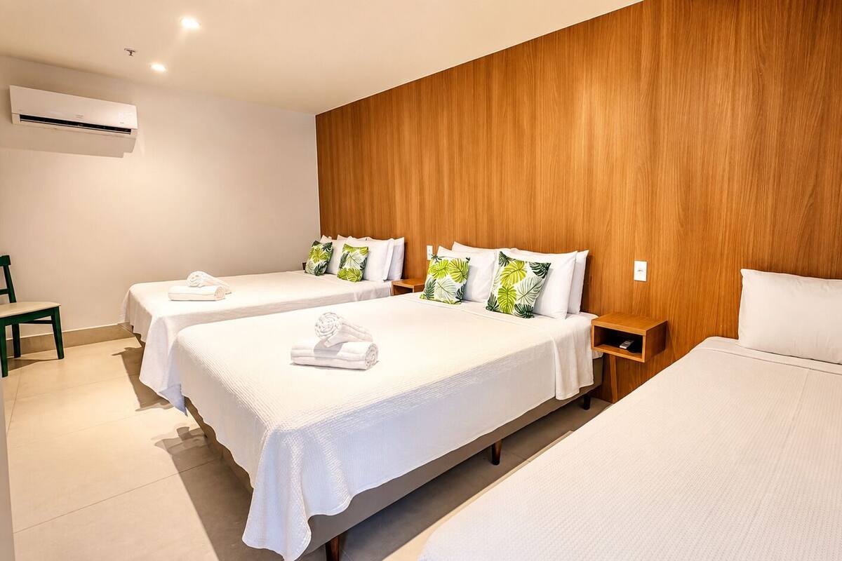 Een hotelkamer met twee enkele bedden, een houten hoofdbord, een airconditioning en een klein nachtkastje.