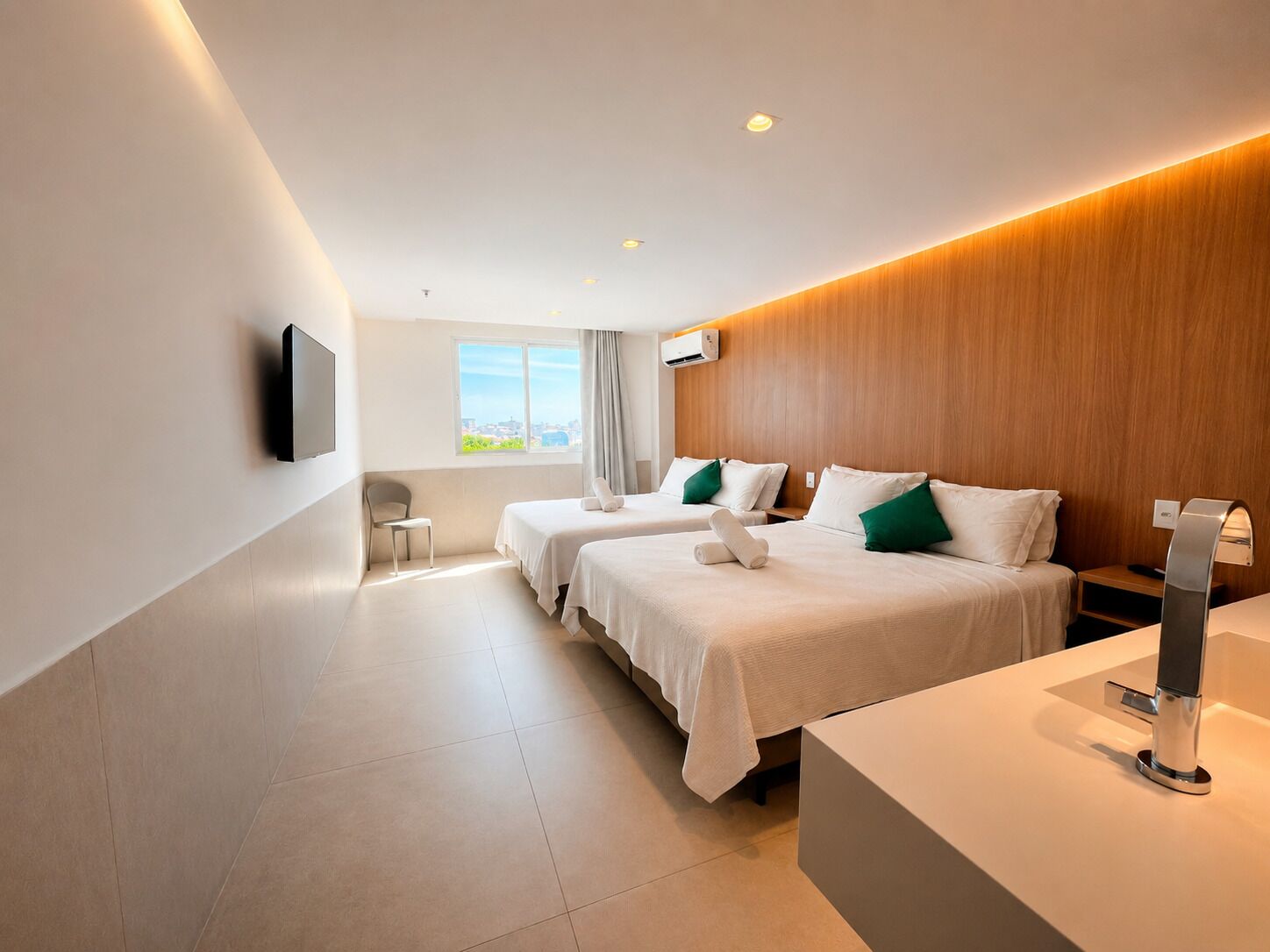 A modern hotel room with two beds, a desk, a chair, a TV, and a window with a city view.
