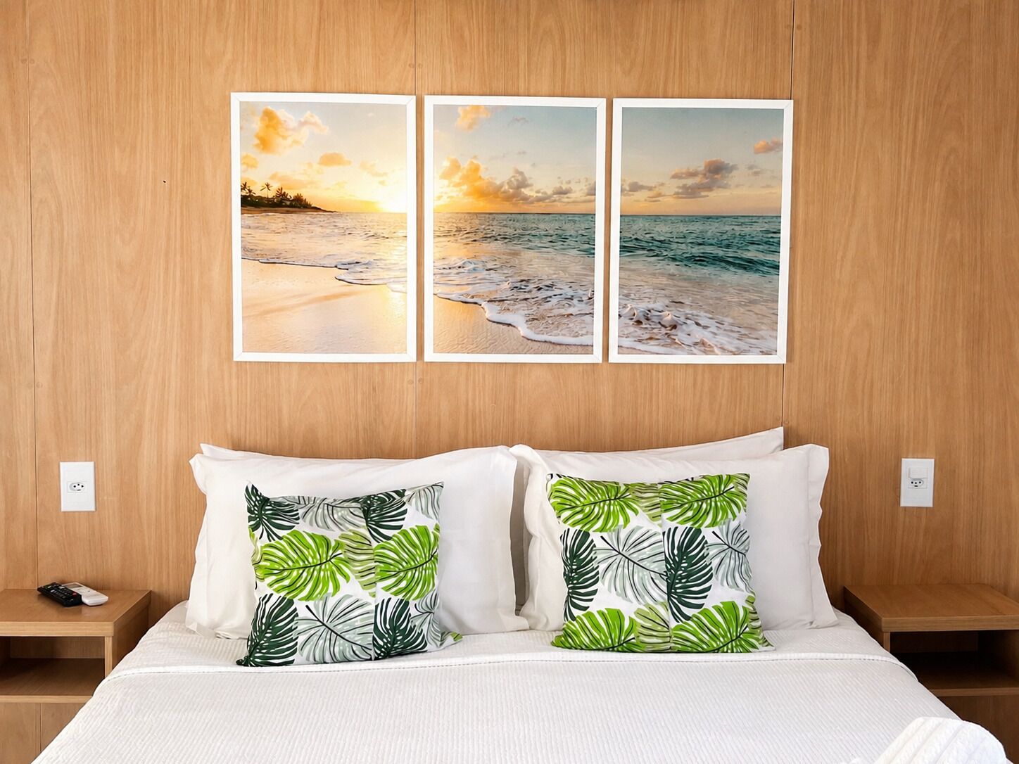 A hotel room with a wooden headboard, a bed with white bedding, two nightstands, and three framed pictures of a beach scene.