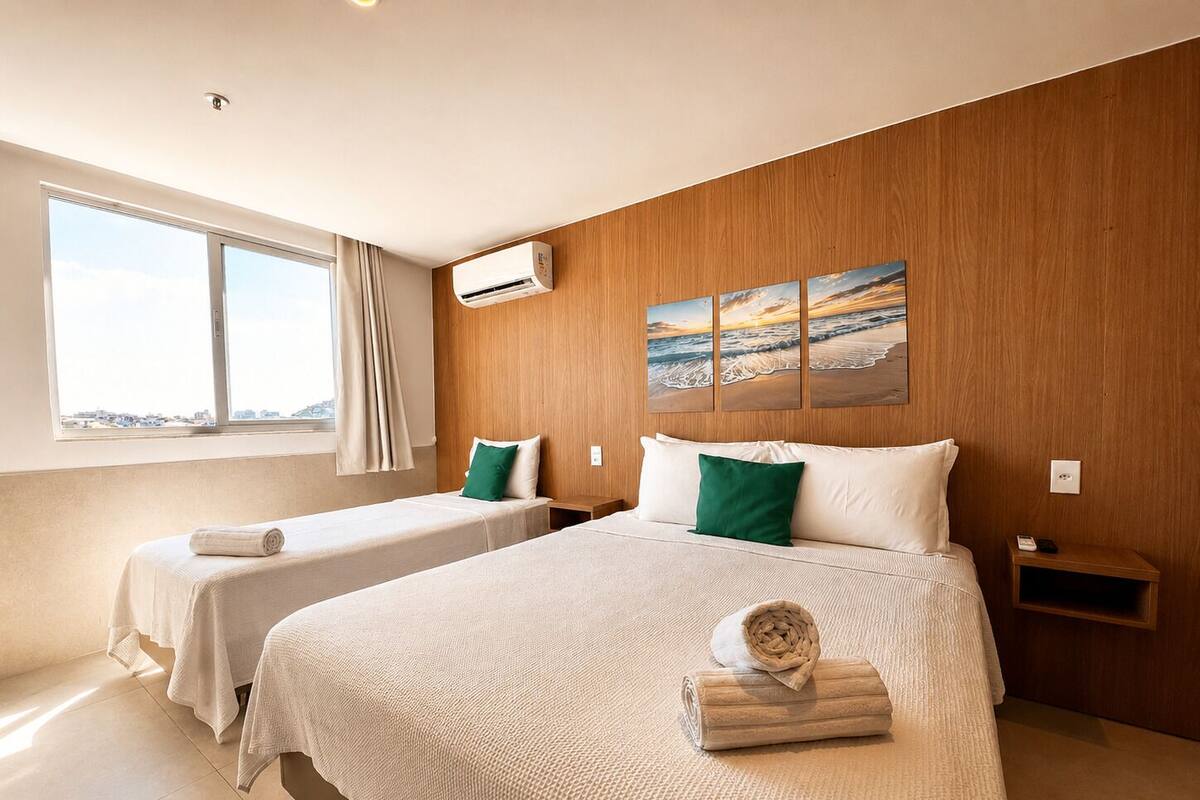 Een hotelkamer met twee bedden, een groot raam, een airconditioning en een schilderij van een strandgezicht.