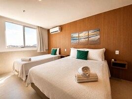Camera d'albergo con due letti, un'ampia finestra, un condizionatore d'aria e un quadro raffigurante una spiaggia.