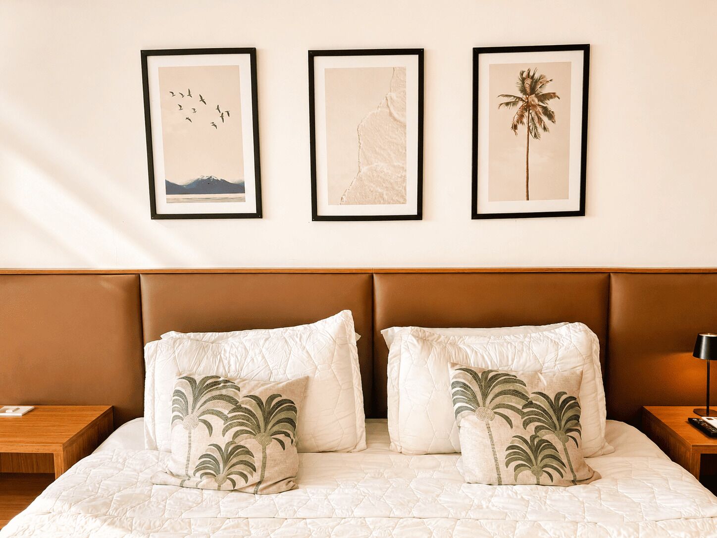 A bed with two pillows, a wooden headboard, and three framed pictures on the wall.