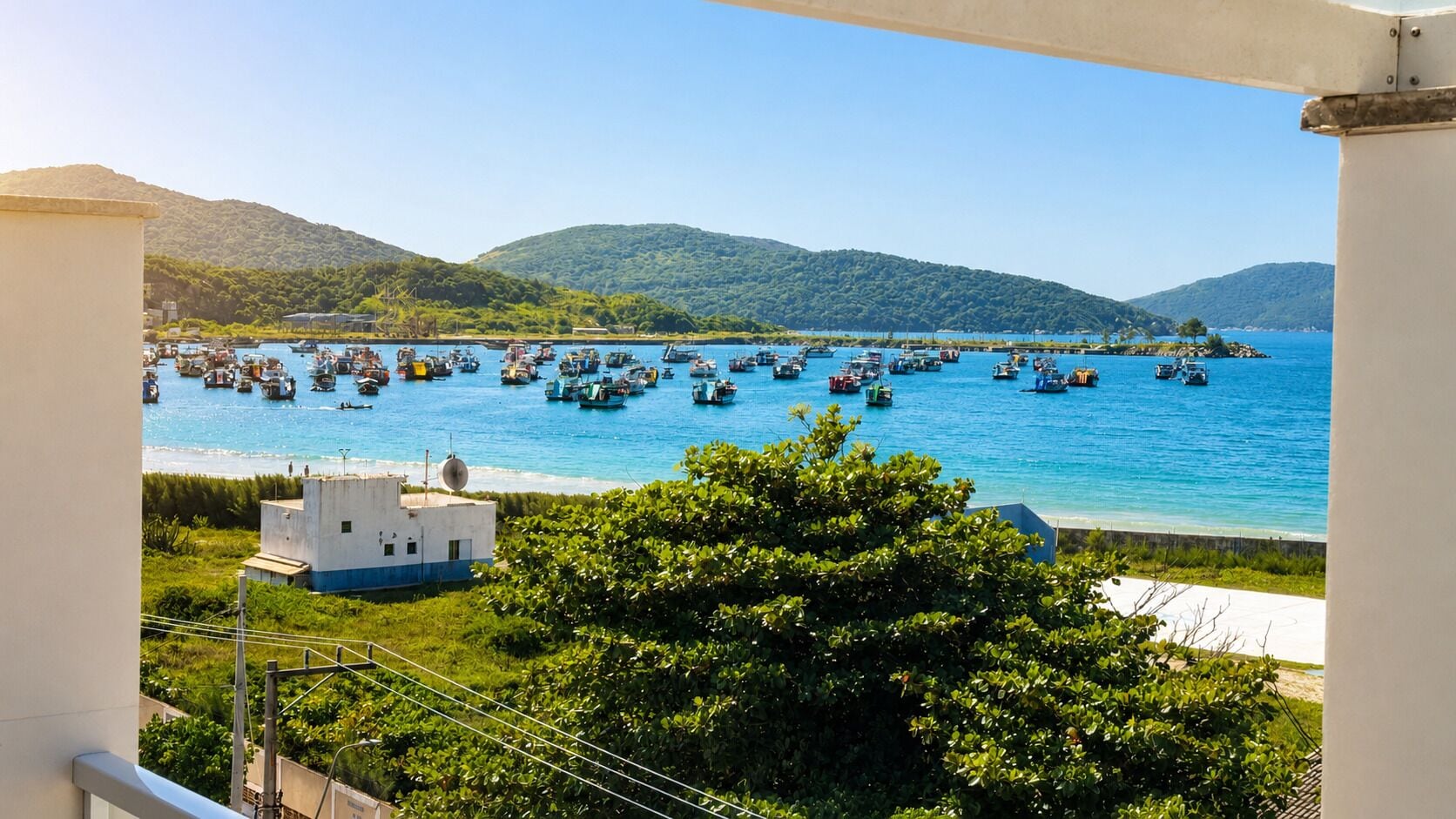 Une vue sur la côte, avec des bateaux, un petit bâtiment blanc et des collines verdoyantes.