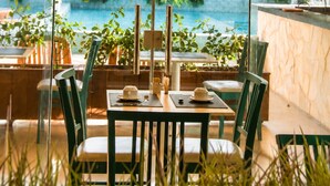 Un restaurante con vistas a una piscina y follaje, con mesas y sillas.