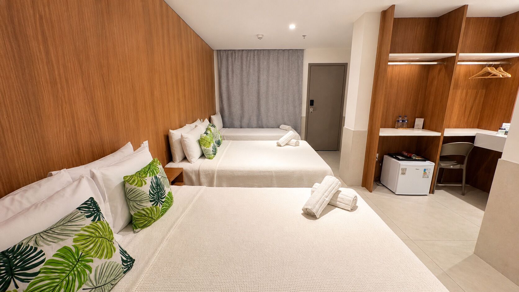 Ein Hotelzimmer mit zwei Betten, einem Kleiderschrank, einem Schreibtisch und einem Kühlschrank.
