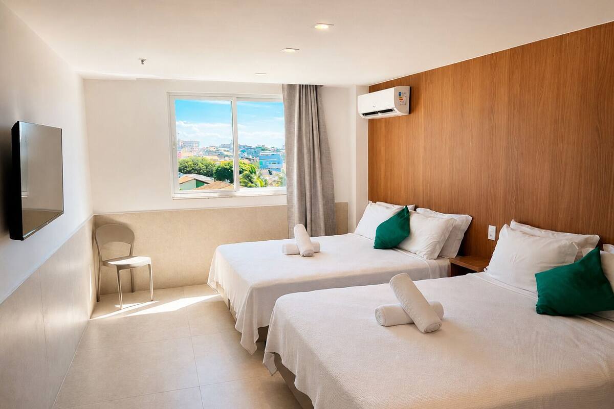 Een hotelkamer met twee bedden, een televisie, een raam met uitzicht op de stad en een airconditioning.