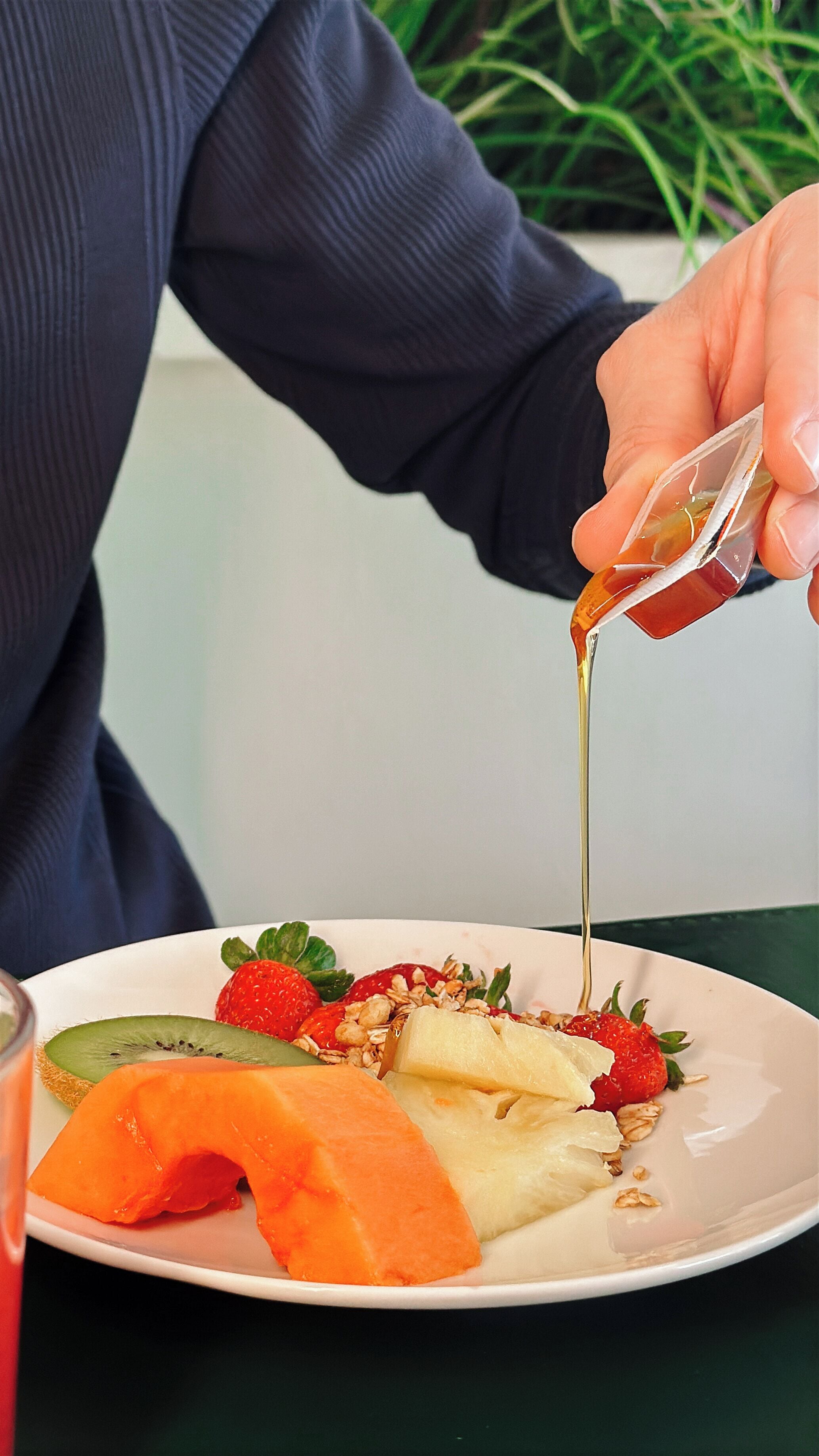 A hand pouring syrup over a fruit salad on a plate.