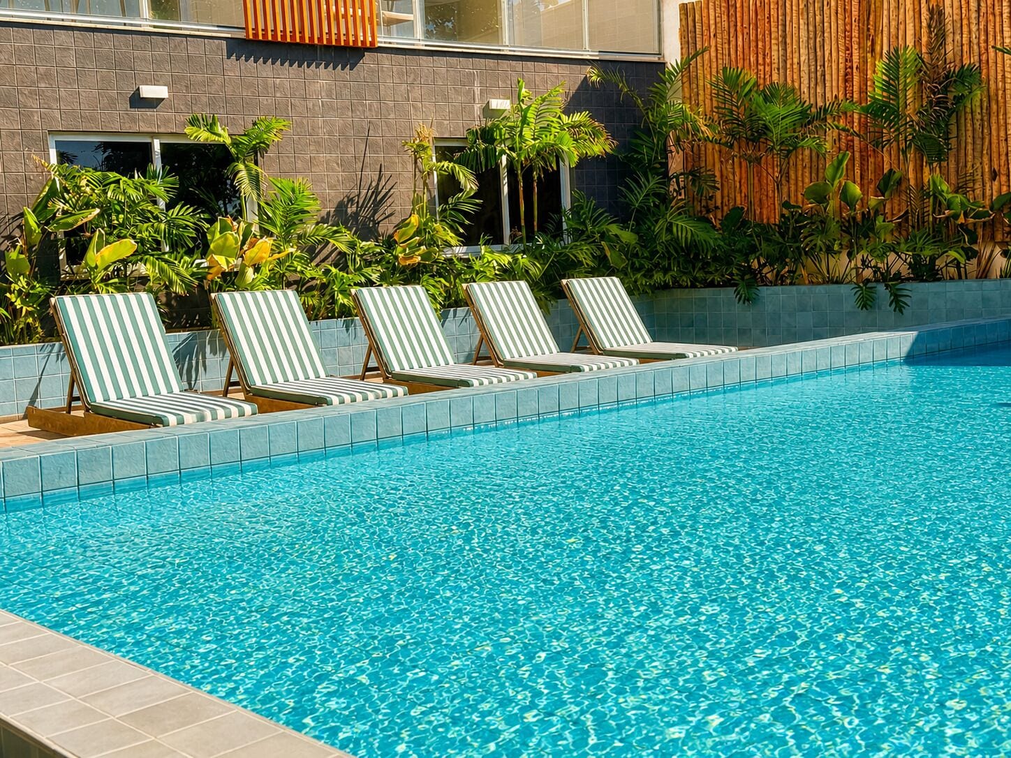 Una piscina con cuatro sillones reclinables a rayas, colocados a lo largo del borde.