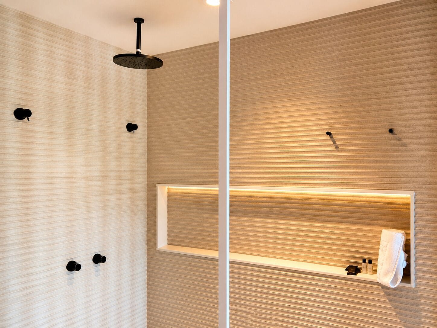 A modern bathroom with a shower, a mirror, and a shelf with toiletries.