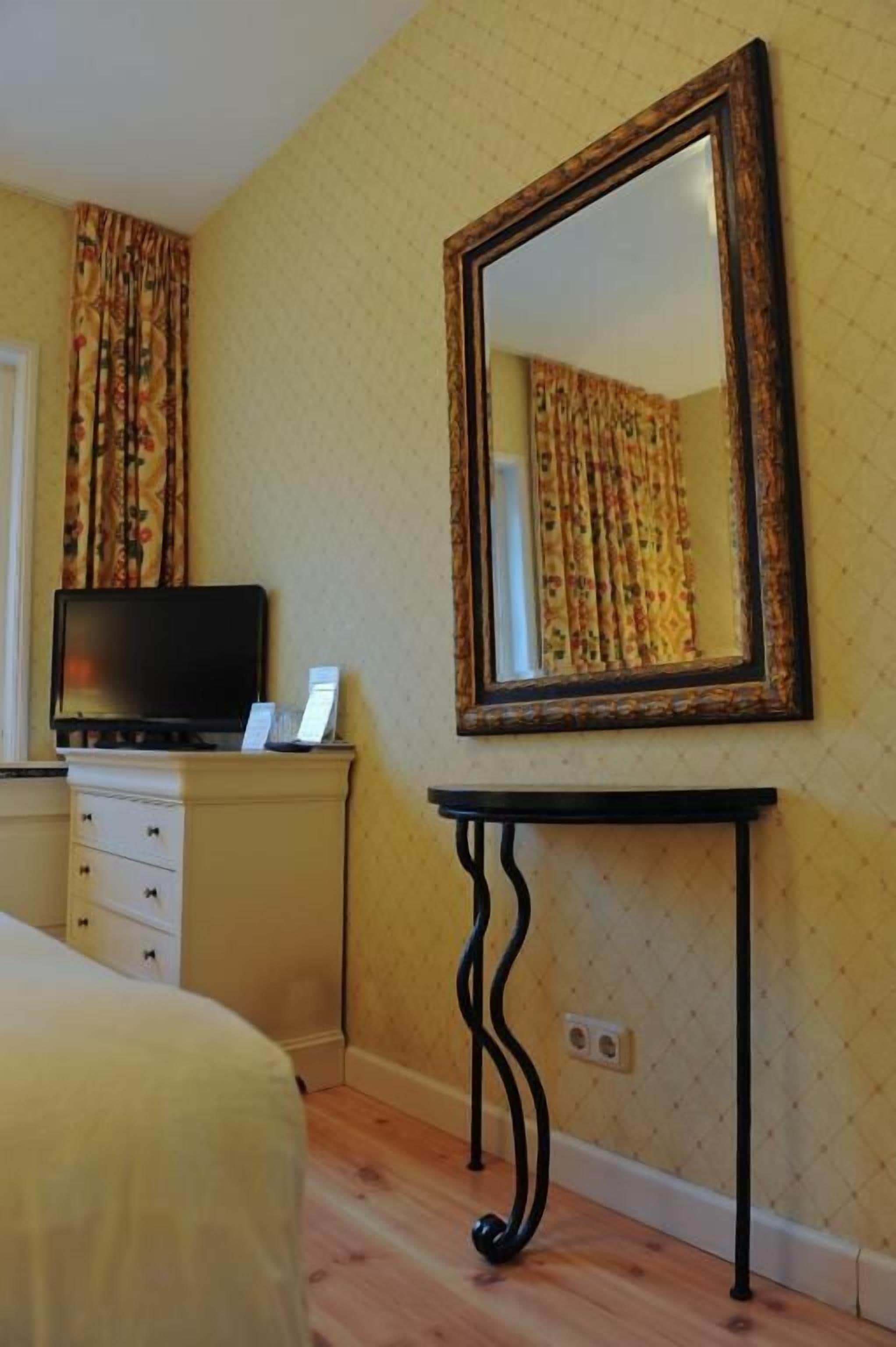 A hotel room with a bed, a television on a dresser, a large mirror, and a patterned wall.