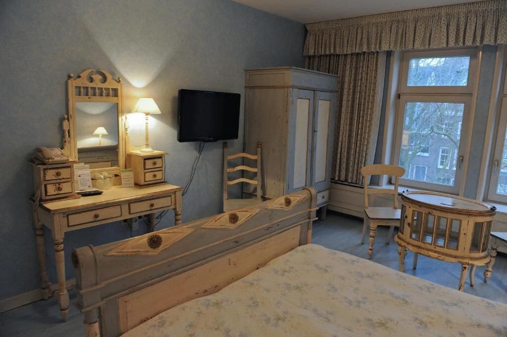 A bedroom with a bed, dresser, mirror, television, and a window with curtains.