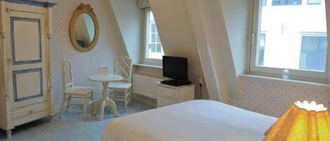 A bedroom with a bed, a desk, a chair, a television, and a window.