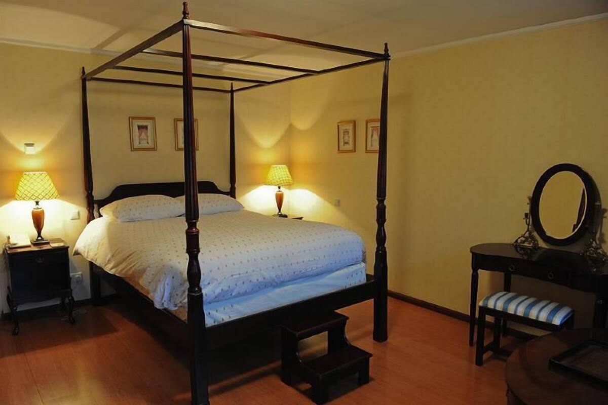 A four-poster bed with a wooden frame, two bedside tables with lamps, a bench, and a mirror on a dresser.