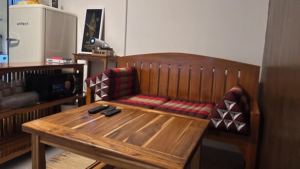 A room with a wooden sofa, a wooden table, a TV, and a refrigerator. - Located at CBD Rama 9 convenience area. Private Room with Share bath (Krung Thep Maha Nakhon)