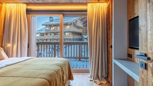 Une chambre à coucher avec un grand lit, un téléviseur fixé à un mur en bois, et un balcon donnant sur un immeuble.