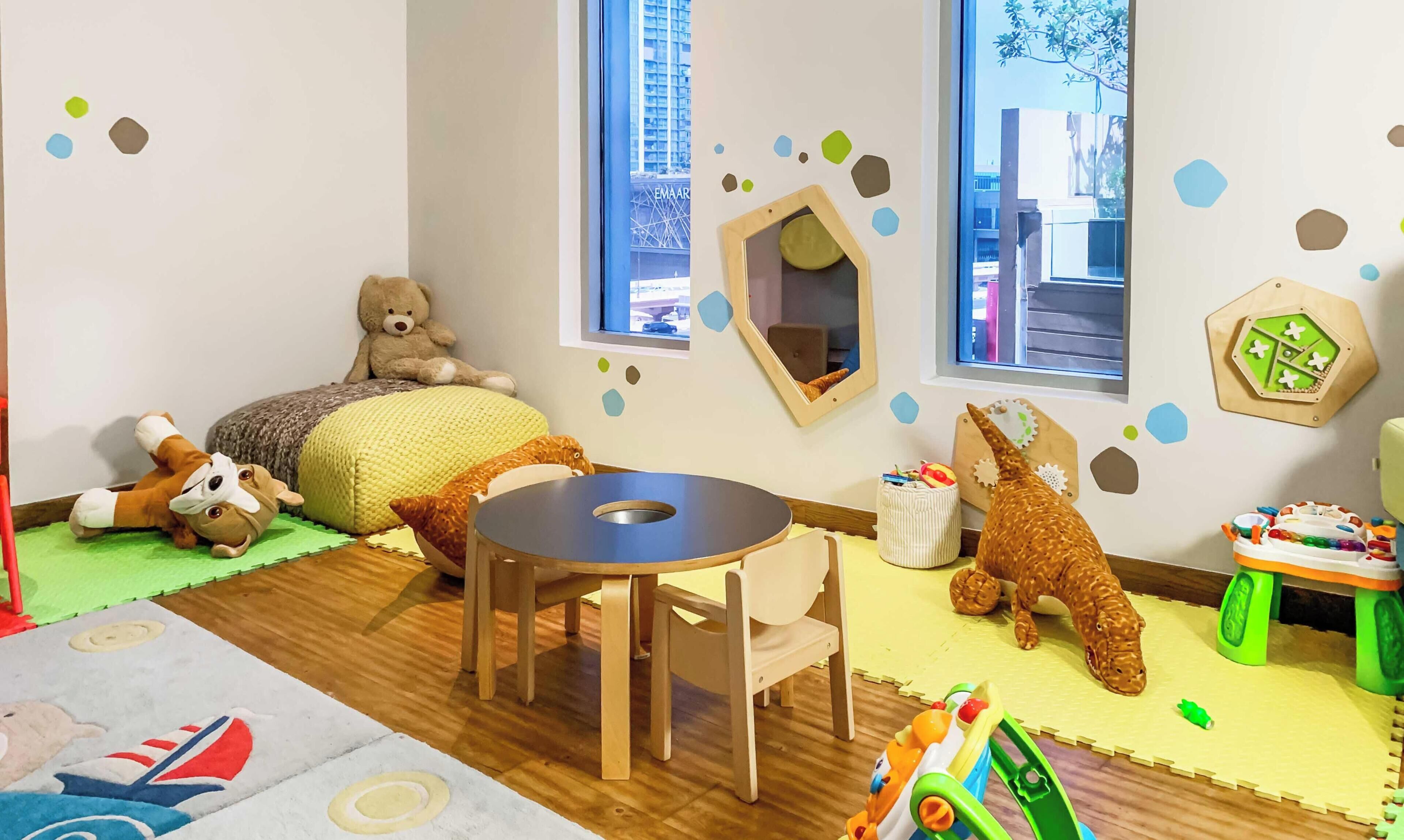 A child's playroom with a round table, bean bag, stuffed toys, and a play area with toys and a toy car.