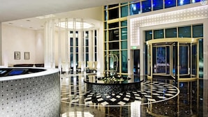 A modern hotel lobby with a reception desk, a central decorative fountain, and a glass elevator. - Paradise View Holiday Homes L.L.C. (Dubai)